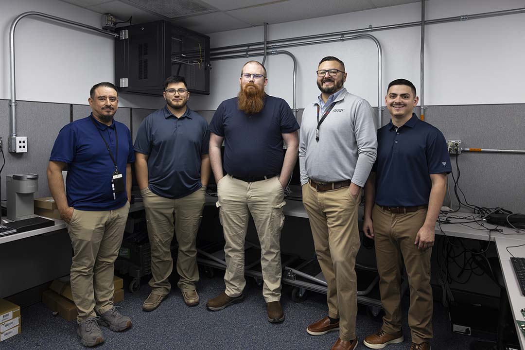 ield Operations Technicians from left to right: Julio Fernandez, Lyvan Alamo, Justin Burr, Keith Hernandez, Adam Landeros Five men stand in a row inside a large cubicle. All are wearing khakis of various shades. Three on the left and the one on the right end are wearing blue, short-sleeved shirts. The man second from the right is wearing a long-sleeved grey sweater. All have dark hair except for the man in the middle who is red-headed.